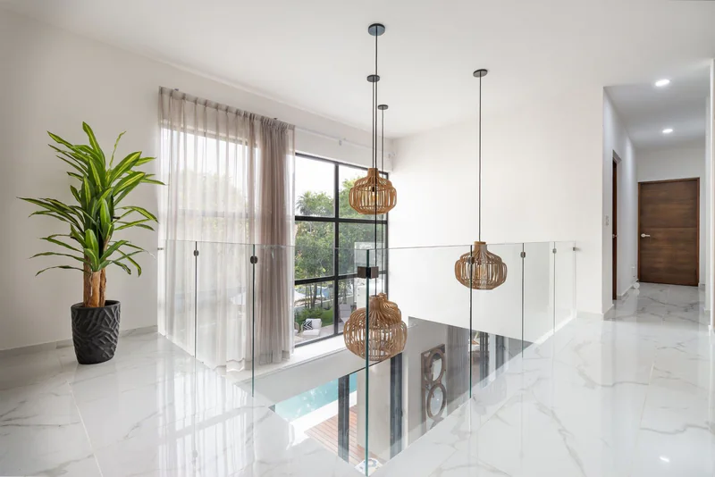 Bright upstairs landing with a glass balustrade, rattan pendant lights and marble floors