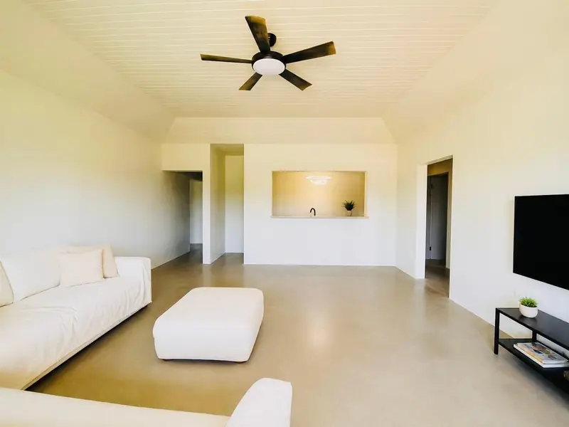 Living room with white sofas, a ceiling fan and a polished concrete floor