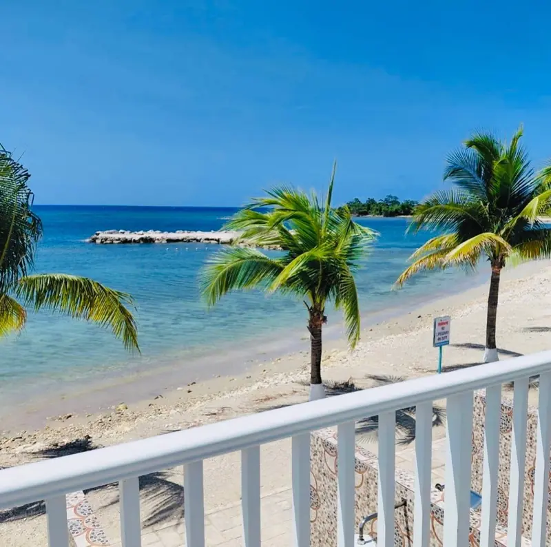 Beach and turquoise water seen over a white balcony rail, with palm trees
